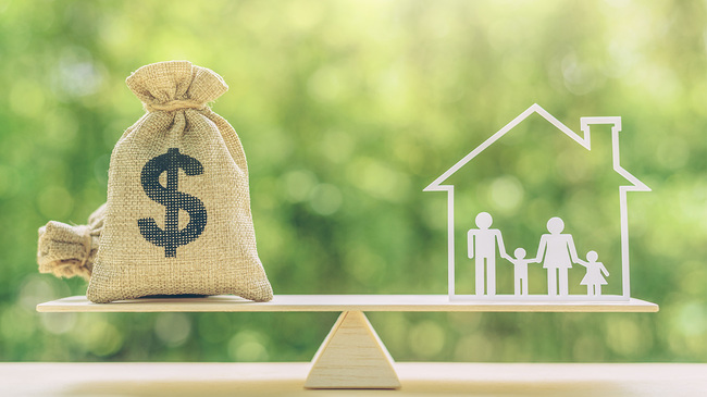 Money bag and family members inside a house on balance scale