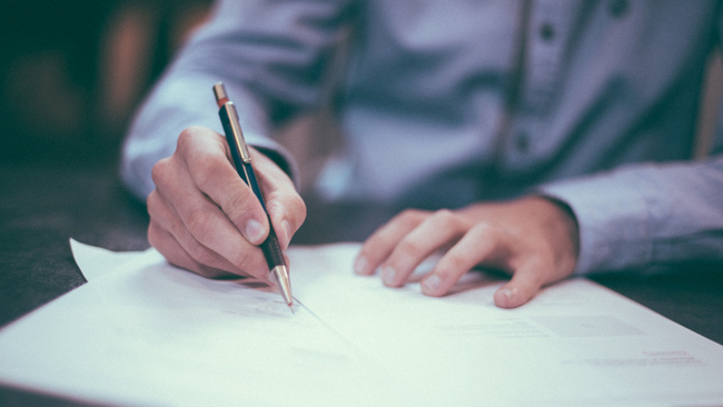 Man using pen to sign loan documents.