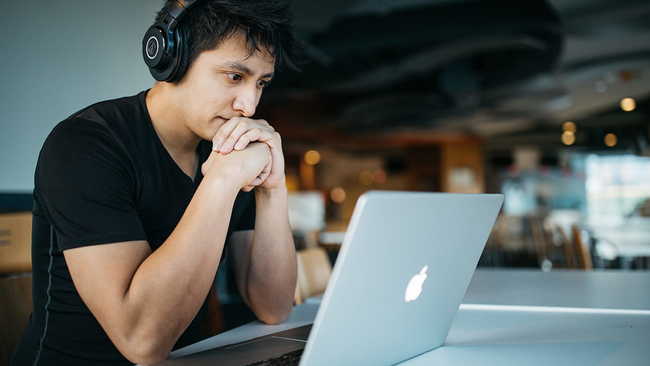 Man wearing headphones while sitting on a chair in front of laptop