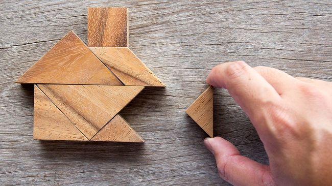 Hand placing puzzle pieces in the shape of a home