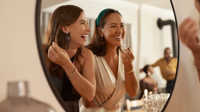 Two friends, standing in front of a mirror, getting ready for a night out