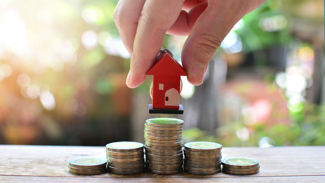 Hand placing red toy house on coin pile