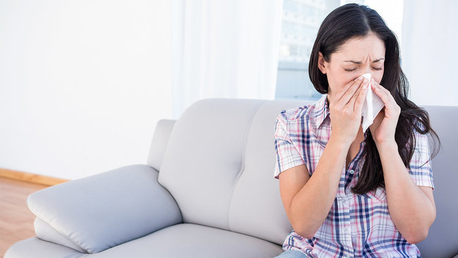 Woman sneezing in living room 