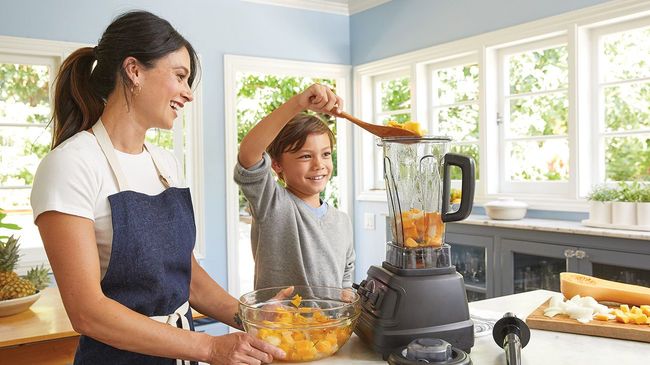 Mother and son laughing in kitchen while making a smoothie