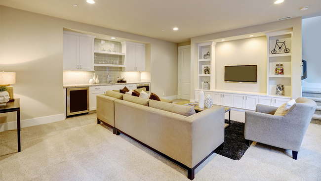 Modern basement with gray sectional, mounted TV,  and wet bar