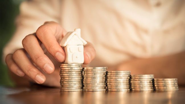 Hand placing toy house on coin pile