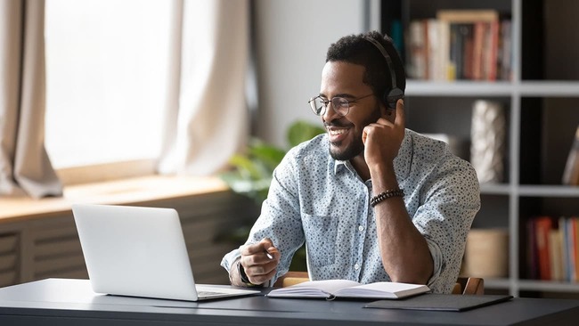 Man sitting at a table smiling at a laptop
