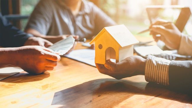 Couple paying mortgage closing costs with agent holding toy home