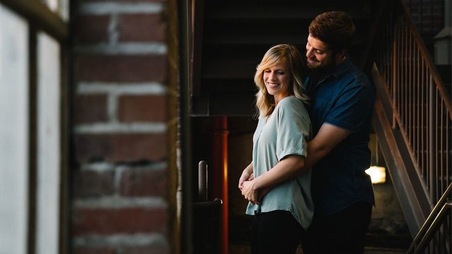 Young couple hugging in front of home window